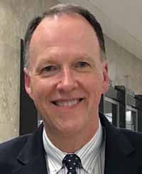 A person in a suit smiling
Description automatically generated